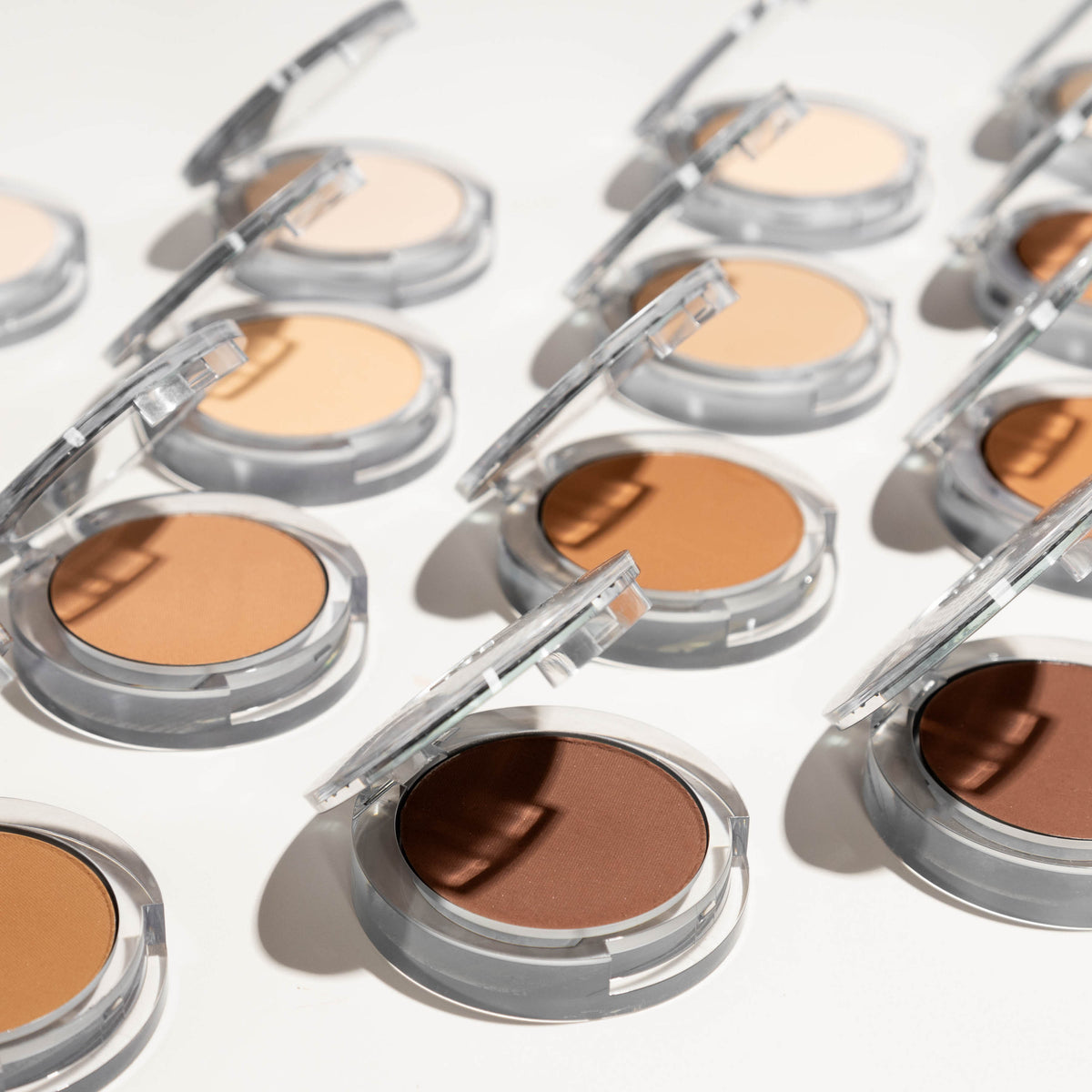 Several 4-in-1 Pressed Mineral Makeup powders arranged in a diagonal pattern against a white table 