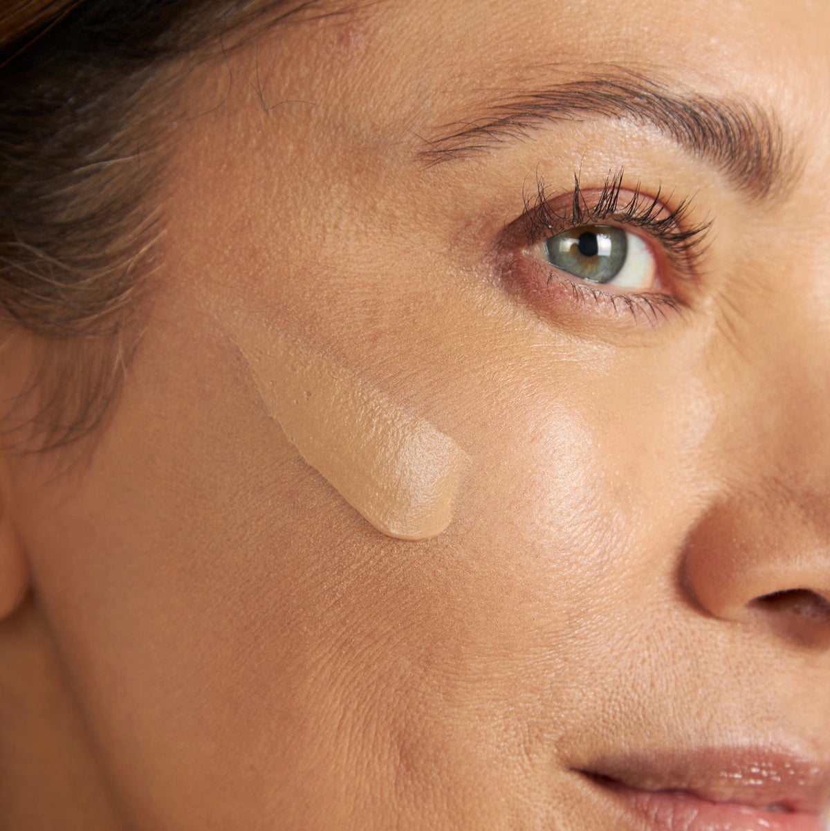Close-up of a woman's cheek with a beige tinted moisturizer swatch illustrating natural coverage.