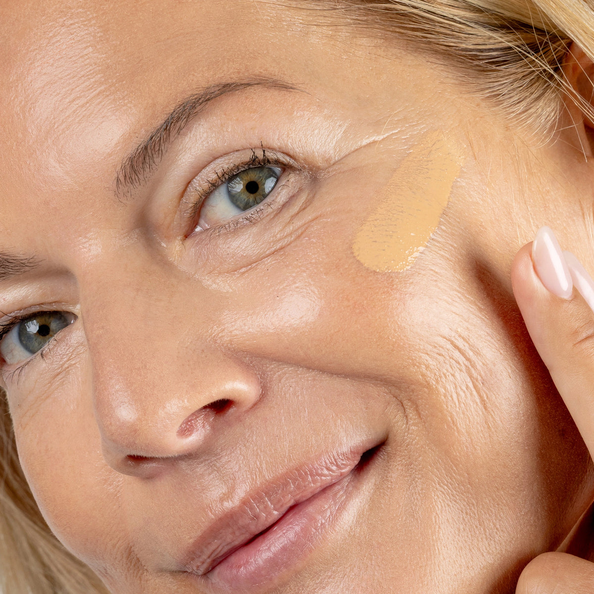 Close-up of a woman applying a beige concealer stick to her face Shade MN4 
