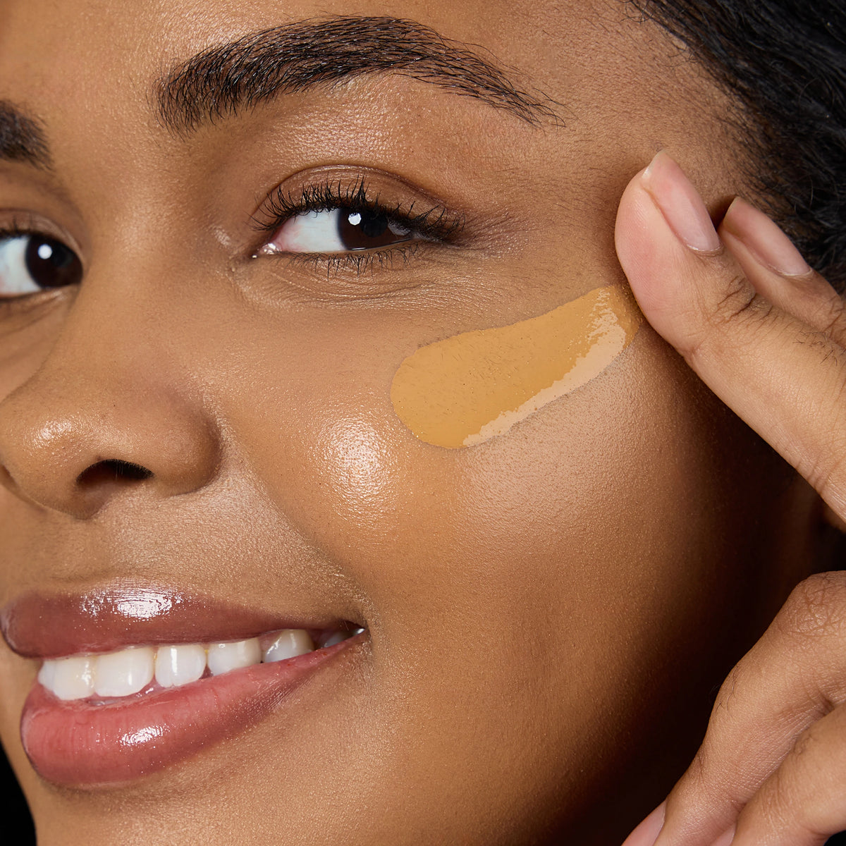 Close-up of a woman applying a beige concealer stick to her face Shade TN7 