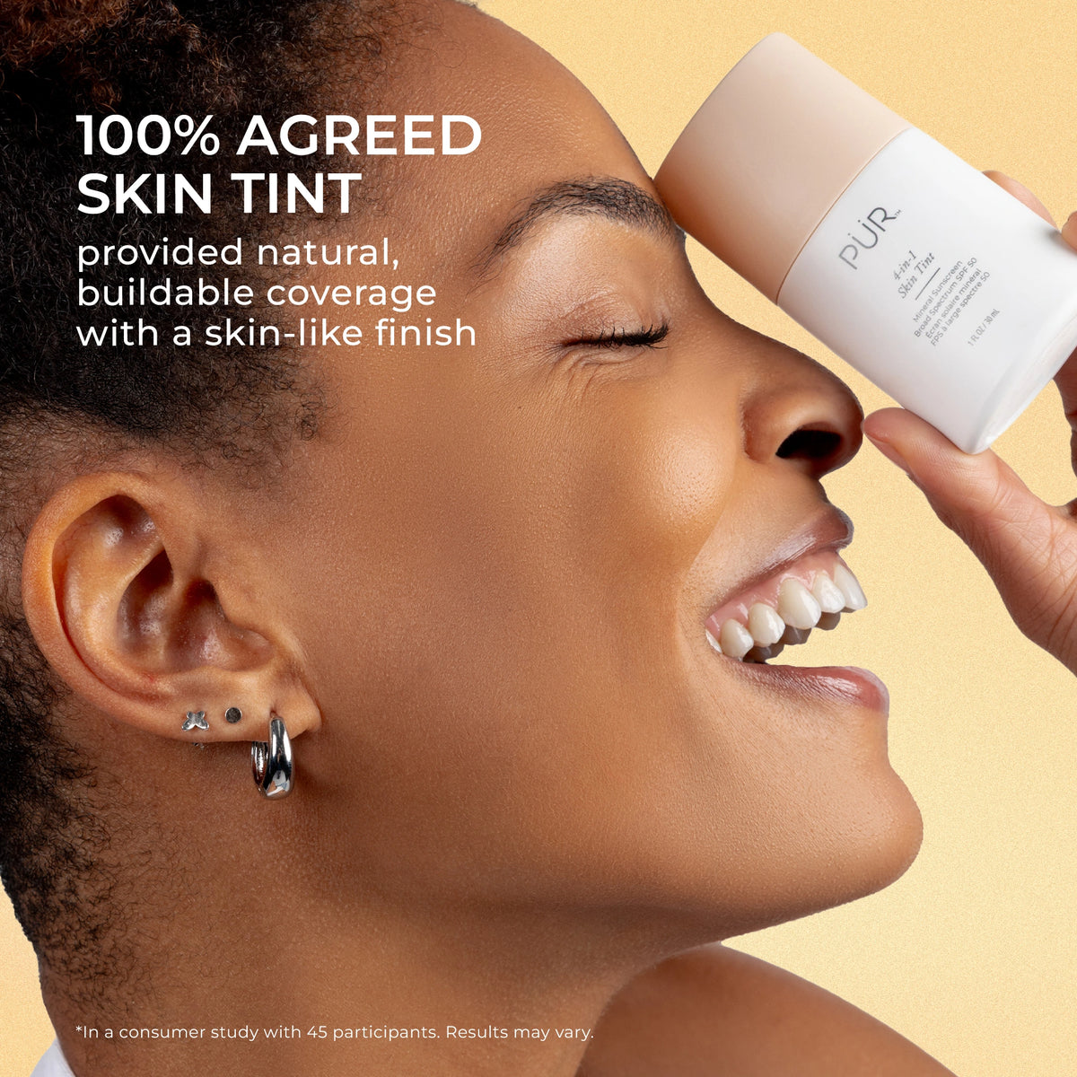 Close-up profile of a smiling woman holding a PÜR 4-in-1 Skin Tint bottle near her forehead to highlight mineral SPF 50 makeup. Independent study found 100% Agreed Skin Tint provided natural, buildable coverage with a skin-like finish.