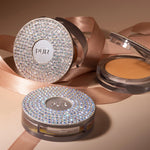 Round PUR pressed mineral makeup compact with sparkling rhinestone lid and beige powder visible, set against pink satin ribbon.
