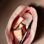 Open pink makeup bag filled with PUR cosmetics including a sparkling round compact, a pink bottle, lip gloss, and a black mascara.