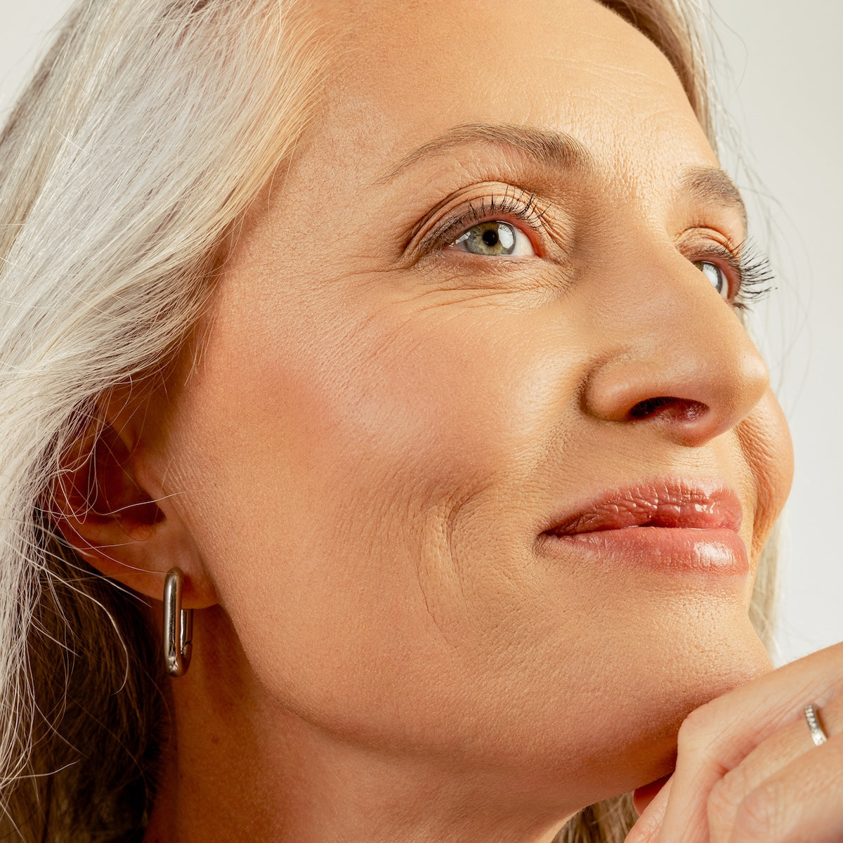 Close up picture of model looking upward with hand on chin against white background.
