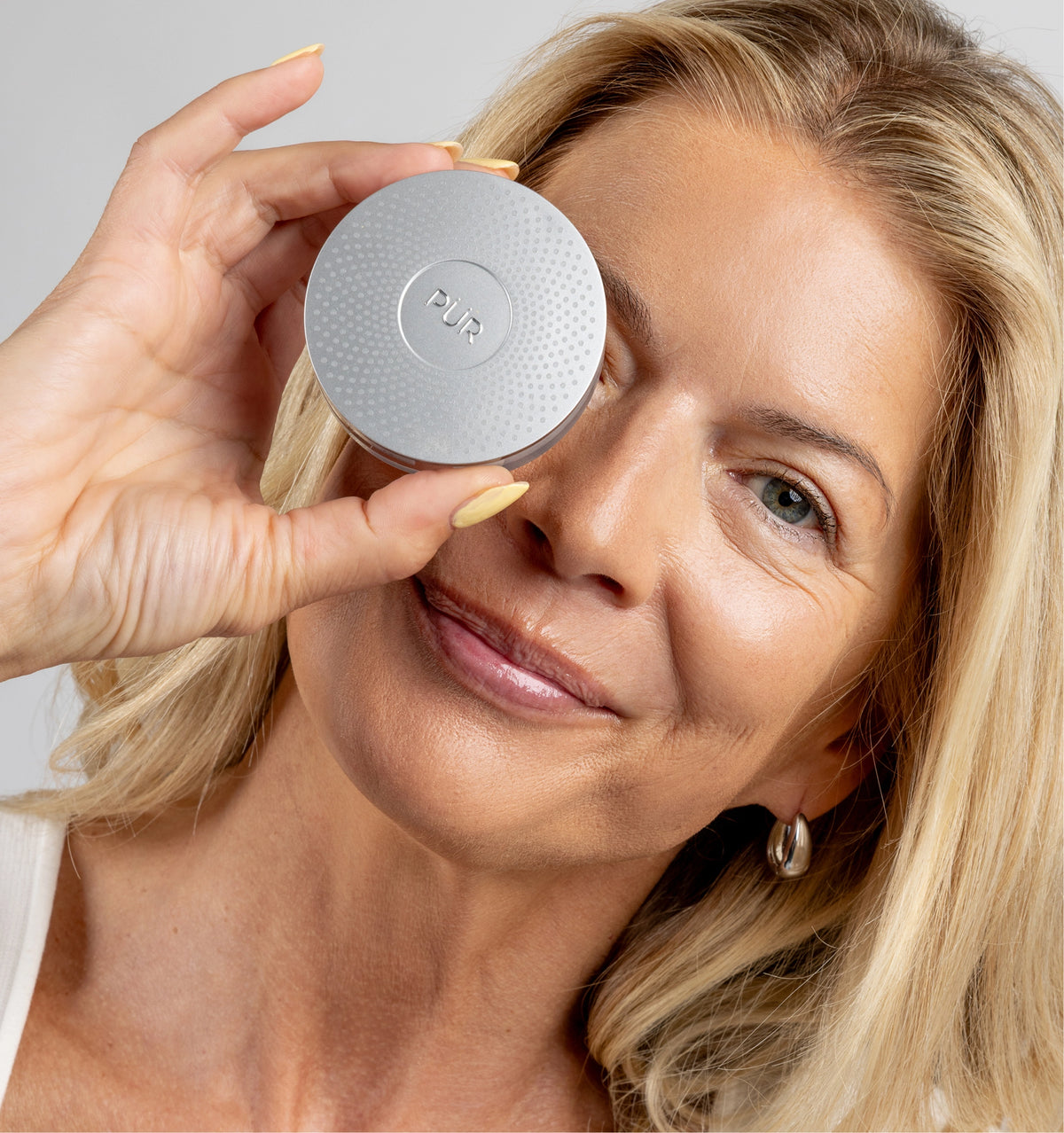 Woman applying a compact powder to her face with a PUR brand logo.