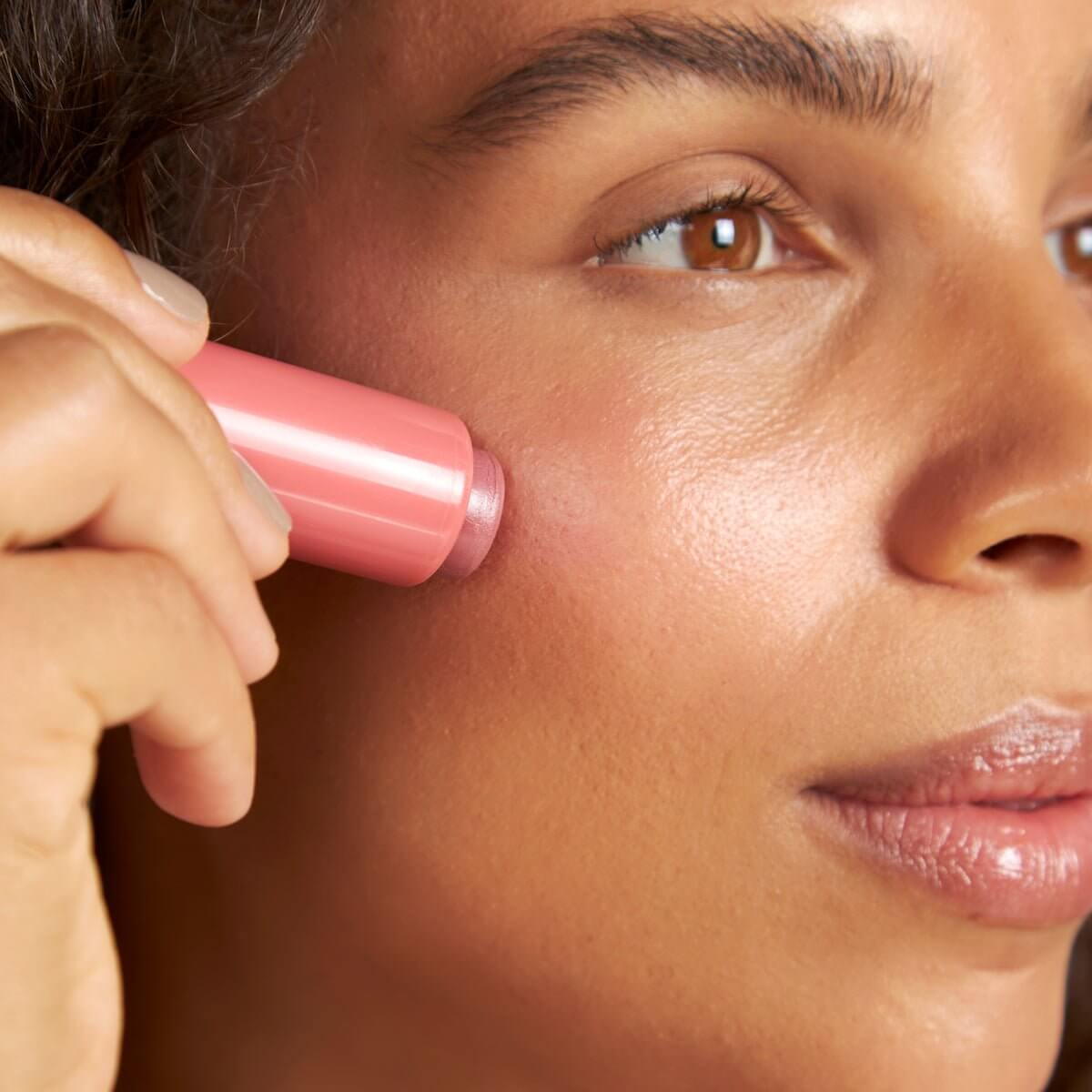 Close-up of a pink Silky Tint Creamy Multitasking Blush Stick with Peptides in Sparkling Rosé shade being applied to the cheek.